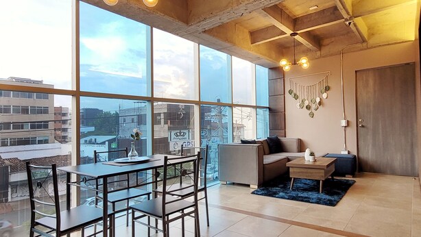 Un salon moderne doté de grandes fenêtres, d’un canapé, d’une table basse et d’un coin repas avec des chaises et une table.
