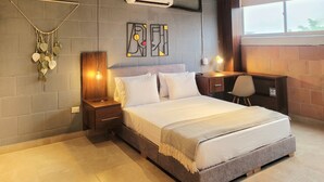 Une chambre moderne avec un grand lit, un bureau et une chaise. Un climatiseur est fixé au mur, et une décoration murale orne la pièce.