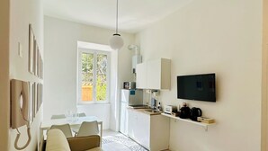 A modern living room with a sofa, a dining area, a kitchen, and a TV mounted on the wall.