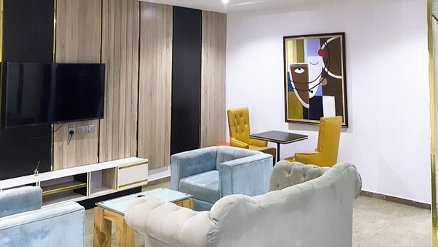 Ein modernes Wohnzimmer mit Flachbildfernseher, einer Couch, zwei Sesseln, einem Couchtisch und einem Gemälde an der Wand.