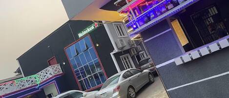 A building with a Heineken sign, a car parked in front, and colorful LED lights on the facade.