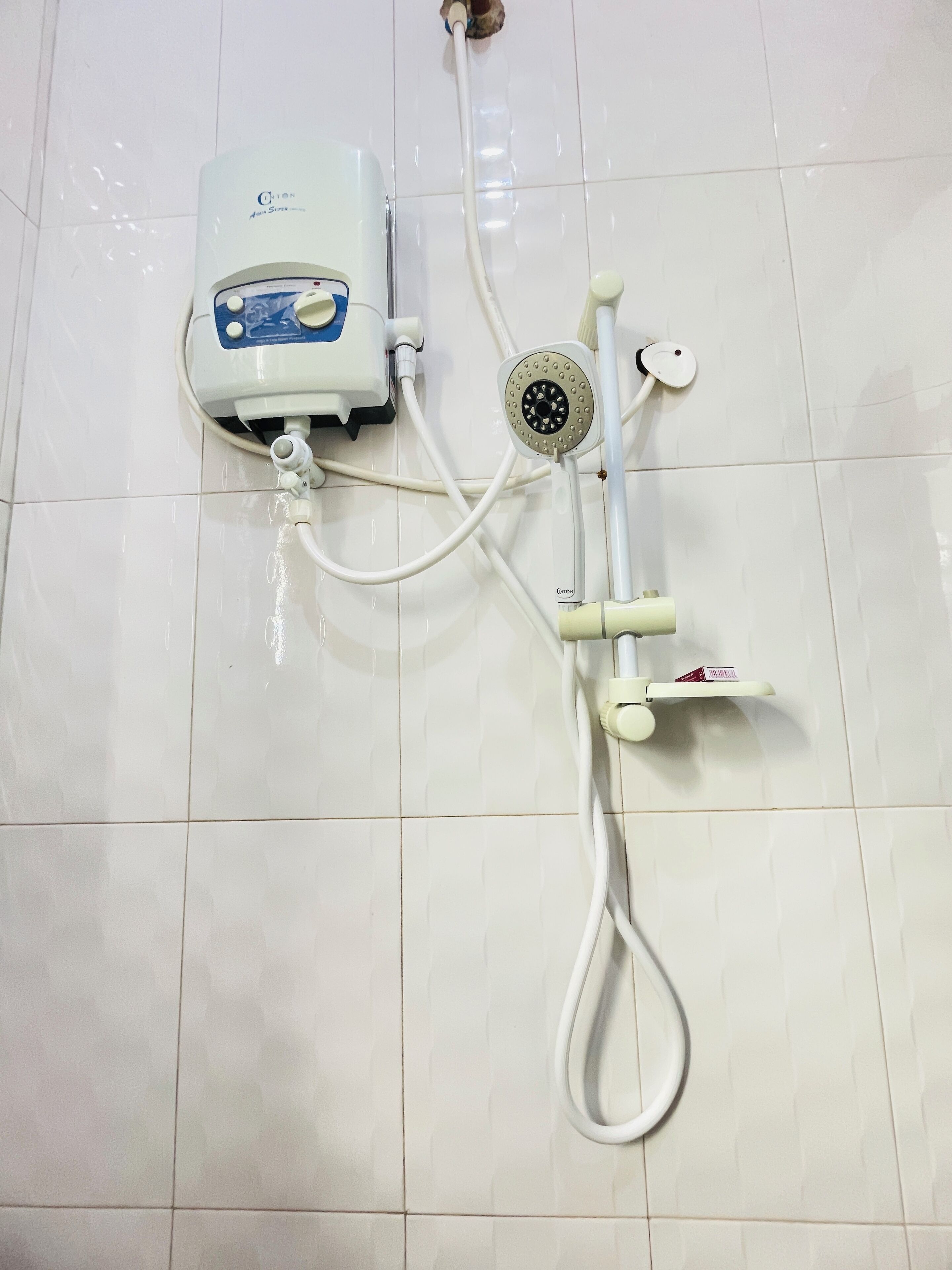 Ein Badezimmer mit weiß gefliestem Boden, einer Handbrause, einem wandmontierten Wasserhahn und einem Durchlauferhitzer.
