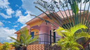 A two-story building with a pink facade, a balcony with a black railing, and potted plants in the foreground. - KDP LODGE KIHONDA (Morogoro)