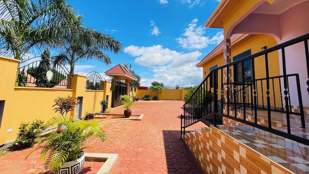 A courtyard with a yellow building, a red-roofed structure, and a gated entrance. - KDP LODGE KIHONDA (Morogoro)