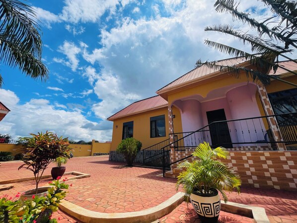 A yellow building with a red roof, a paved courtyard, and potted plants. - KDP LODGE KIHONDA (Morogoro)