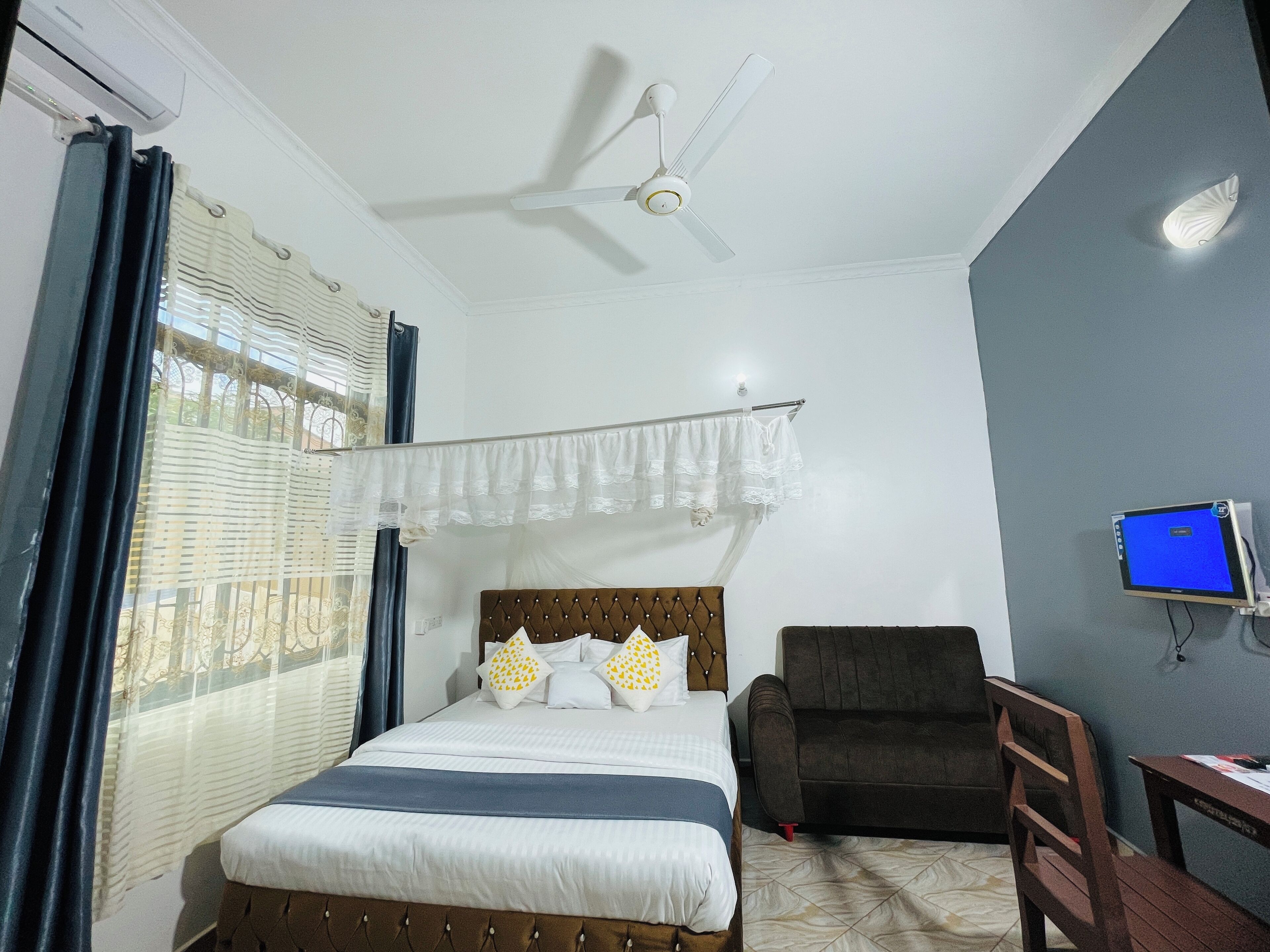 A bedroom with a bed, a chair, a desk, a ceiling fan, and a TV.