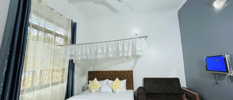 A bedroom with a bed, a chair, a desk, a ceiling fan, and a TV.