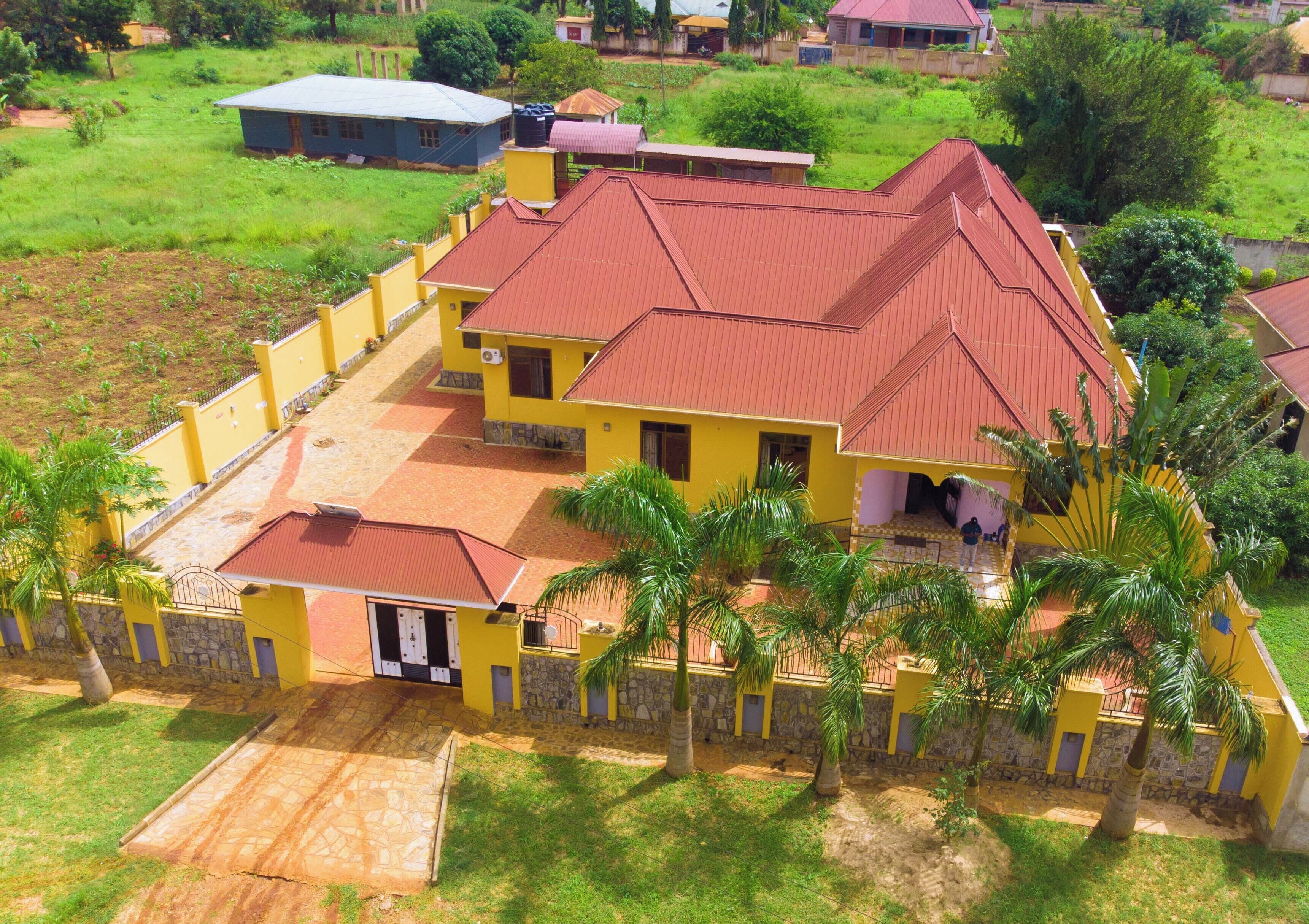 A yellow building with a red roof, surrounded by palm trees and a stone wall.