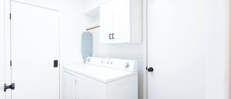A laundry room with a white washing machine, a drying rack, and a cabinet.