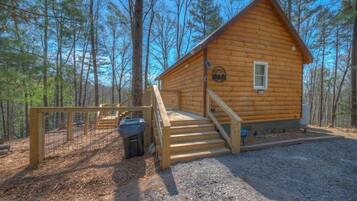 A wooden cabin with a staircase leading to the entrance, surrounded by trees.