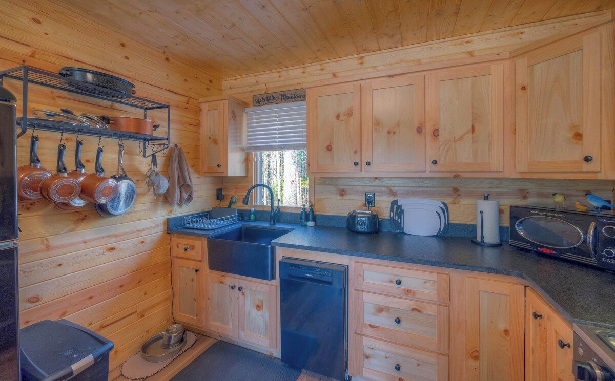 A wooden cabin kitchen with a sink, stove, and hanging pots.