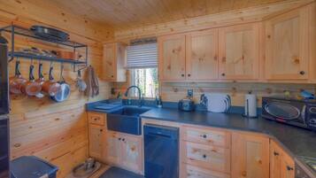 A wooden cabin kitchen with a sink, stove, and hanging pots.