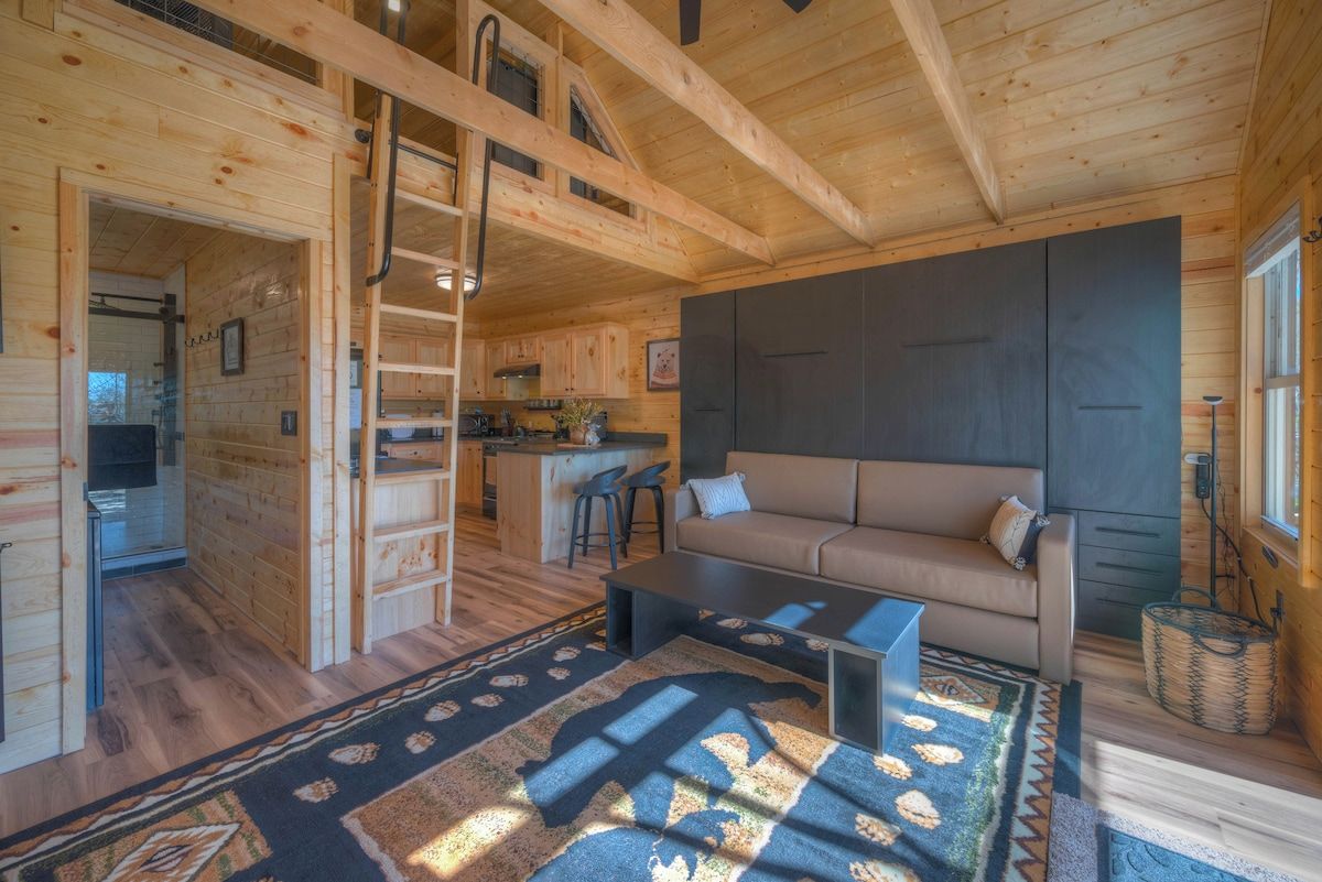 A wooden cabin interior with a sofa, coffee table, and a kitchen area.