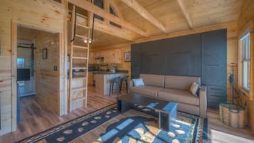 A wooden cabin interior with a sofa, coffee table, and a kitchen area.