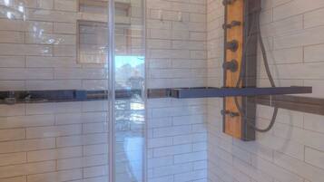 A shower with a glass partition, white tiled walls, and a wooden ceiling.