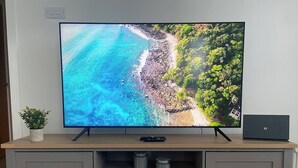 A flat-screen TV on a wooden TV stand with a remote and a laptop beside it.