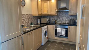A compact kitchen with wooden cabinets, a built-in washing machine, and a tiled backsplash.