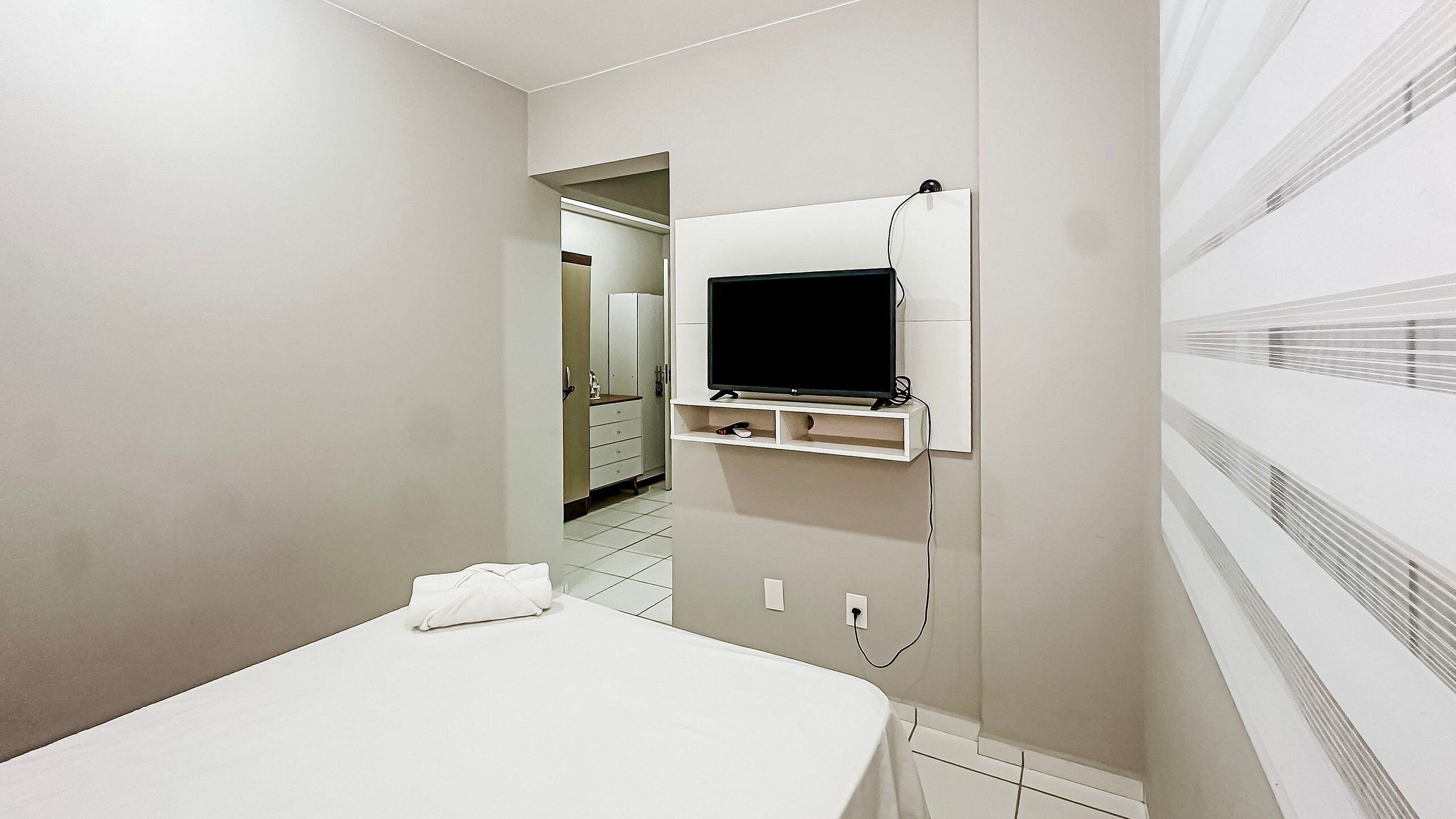 Quarto de hotel com cama, televisão fixada na parede e banheiro visível por uma porta aberta.