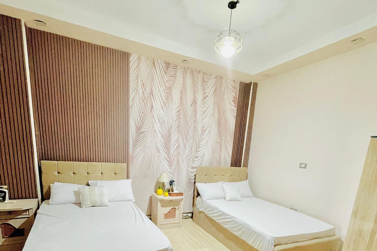 A hotel room with two beds, a nightstand, a lamp, and a decorative wall panel.
