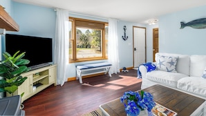 Een woonkamer met een televisie, een bankje, een witte bank en een salontafel.