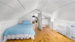 Een slaapkamer met een bed, houten vloer, witte muren en een schuin dak.