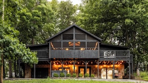 A two-story wooden cabin with a stone foundation, large windows, and a balcony. - Three Bears Cottage: Cozy Wears Valley Cottage (Sevierville)