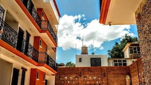 A courtyard with a tiled floor, a brick wall with decorative elements, and a water tank on a building in the background. - Hotel Boutique Casa de las Flores     (Huajuapan)