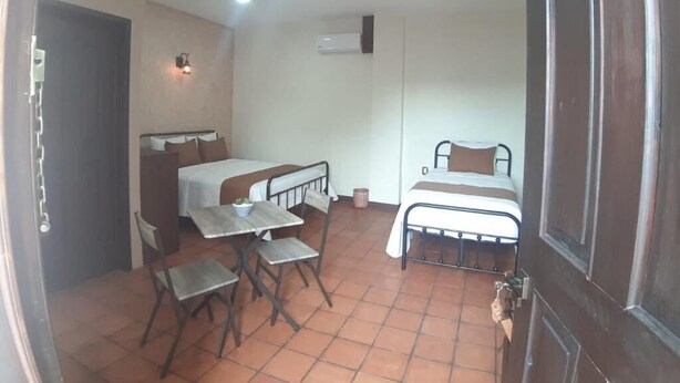 A small, compact room with a bed, a desk, and a chair. There is a door on the right and an air conditioning unit on the wall. - Hotel Boutique Casa de las Flores     (Huajuapan)