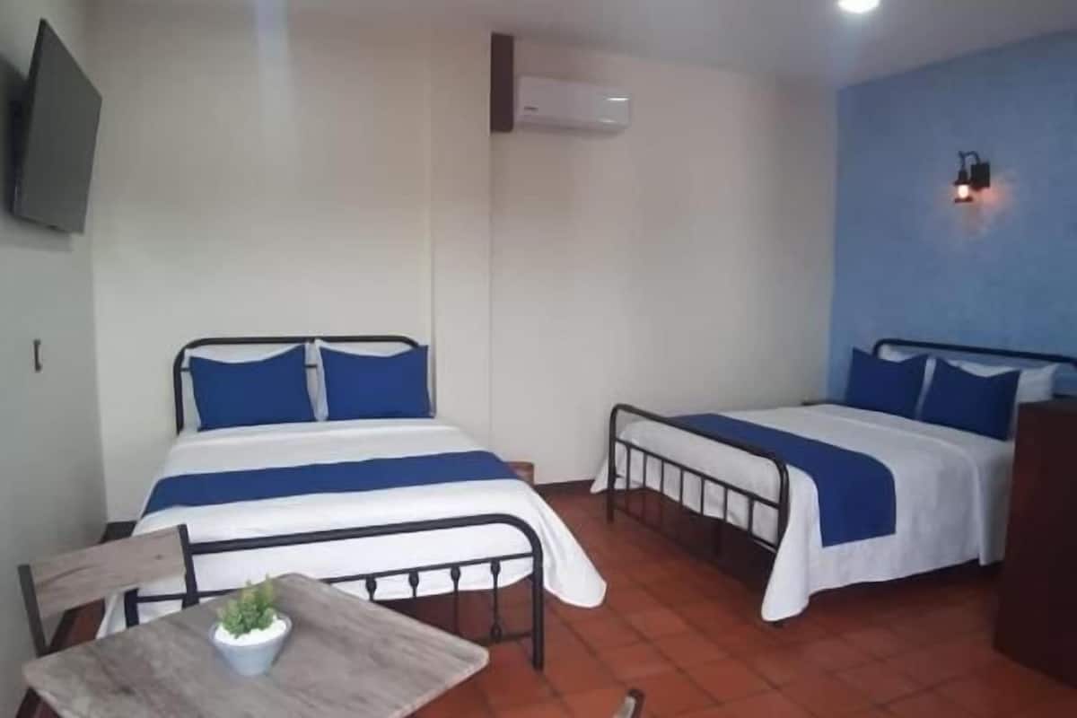 Une chambre avec deux lits, une table, des chaises, un téléviseur et un appareil de climatisation.