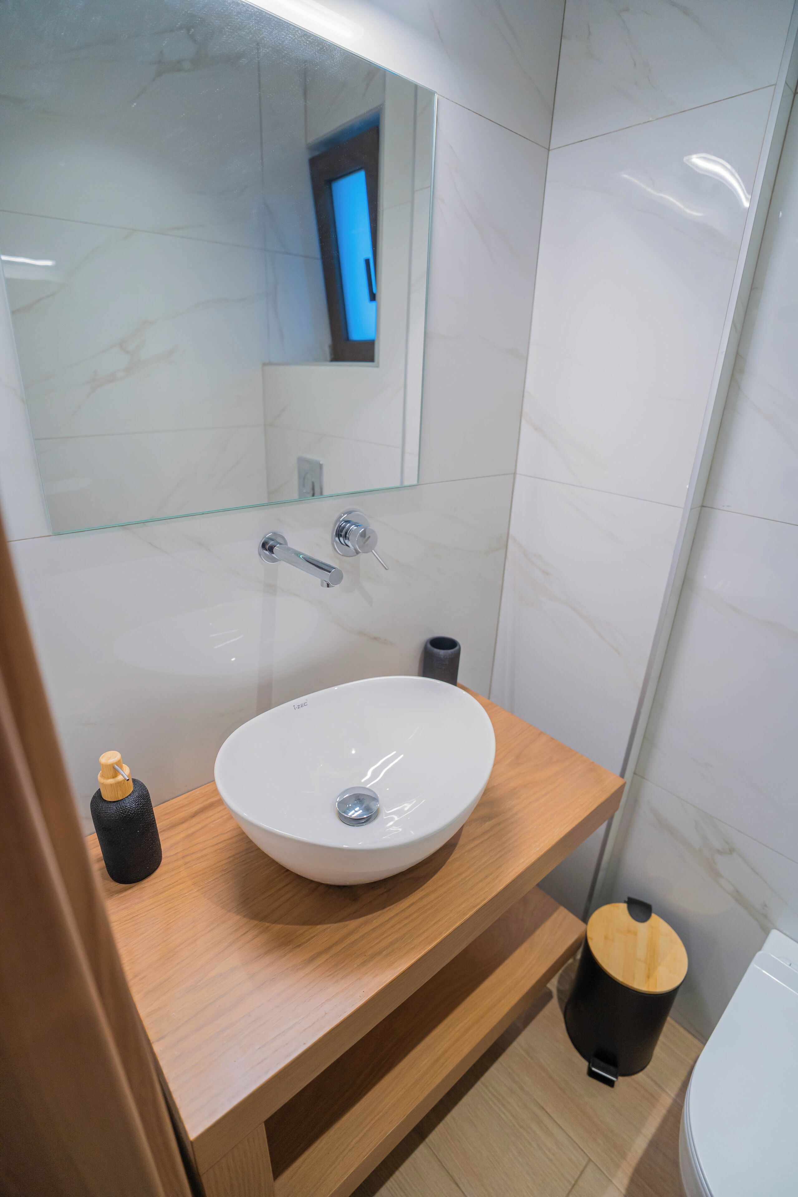 A modern bathroom with a white sink, wooden vanity, and a glass shower enclosure.