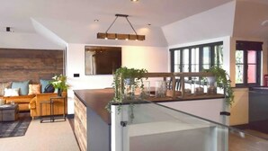A modern interior with a wooden accent wall, a glass railing, and a dining area with plants. - Captains Loft (Falmouth)
