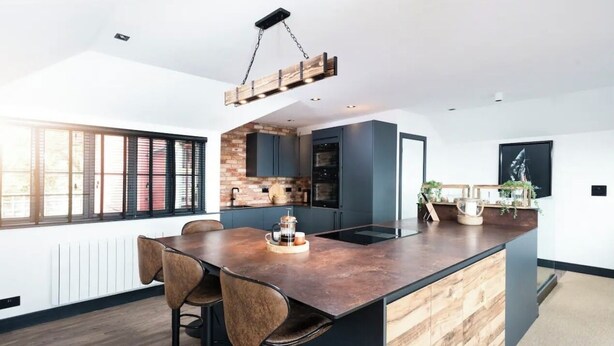 A modern kitchen with a central island, dark cabinetry, and a brick accent wall. - Captains Loft (Falmouth)