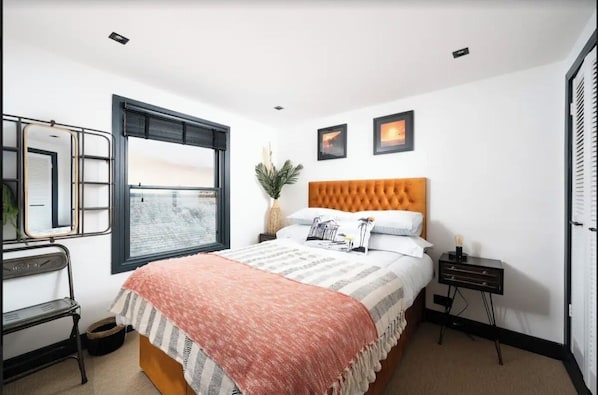 Een slaapkamer met een groot bed, een raam, een nachtkastje en een spiegel.