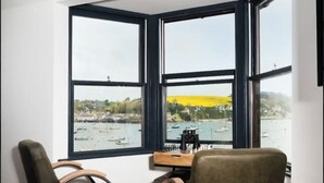 A room with a large bay window overlooking a harbor, two leather chairs, and a small desk with a chessboard. - Captains Loft (Falmouth)