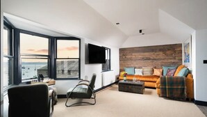 A living room with a large window, a sofa, a chair, and a flat-screen TV. - Captains Loft (Falmouth)