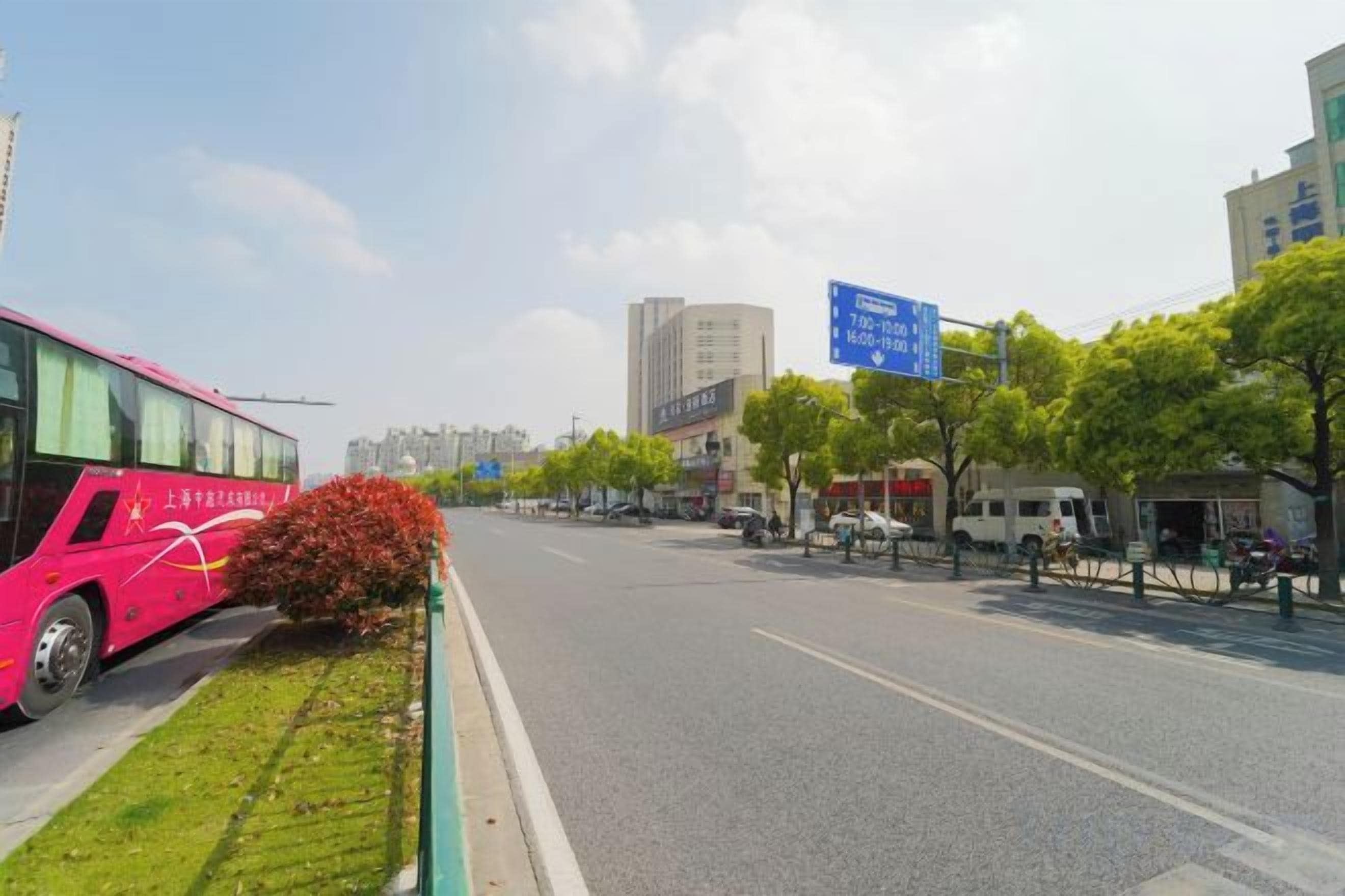 A street with a pink bus parked on the left, a clear sky, and buildings in the background.