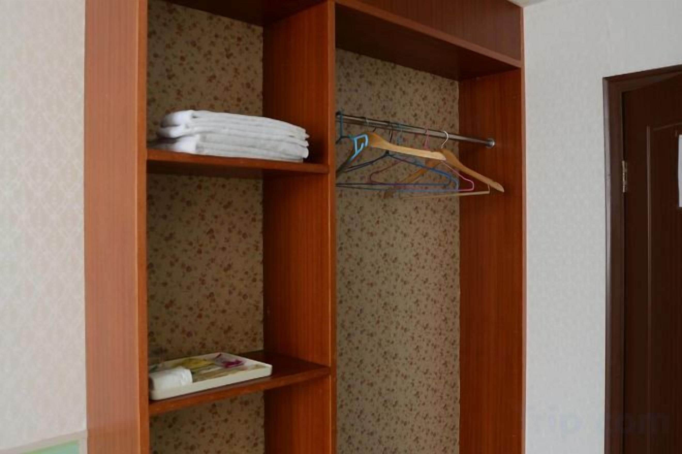 A wooden closet with shelves, one holding folded towels and another with a hanging rack.