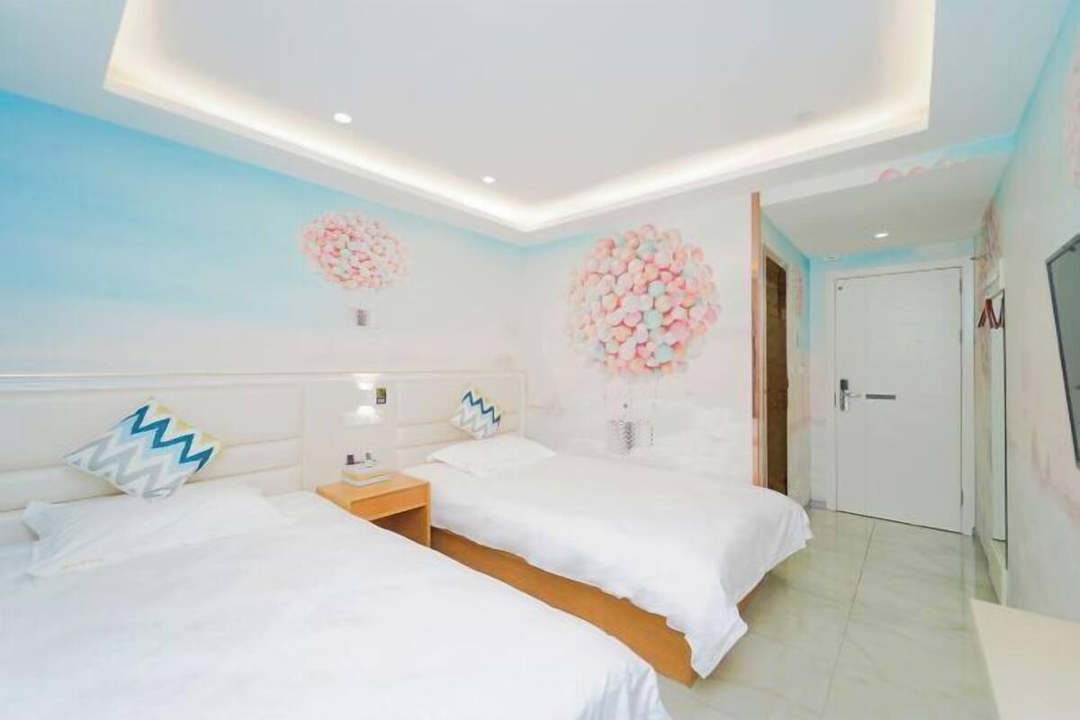 A hotel room with two beds, a nightstand, a wall-mounted TV, and a door leading to another room.