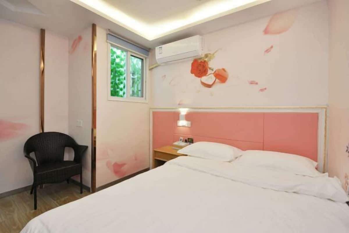A hotel room with a bed, a chair, a nightstand, a window, and an air conditioning unit.