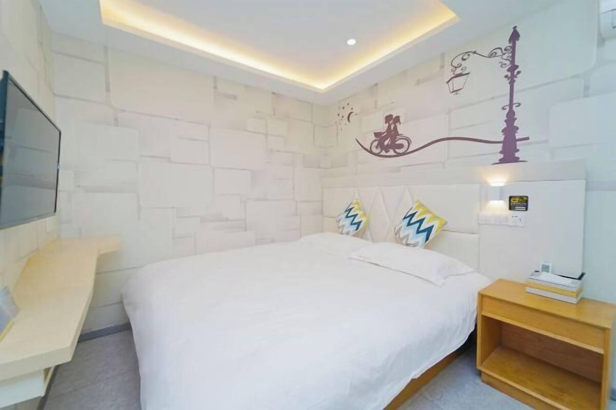 A modern hotel room with a large bed, a bedside table, a TV, and a decorative wall.