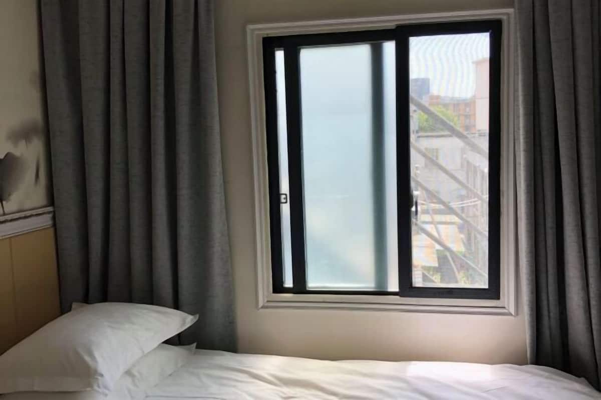 A hotel room with a bed, a window with curtains, and a view of buildings outside.