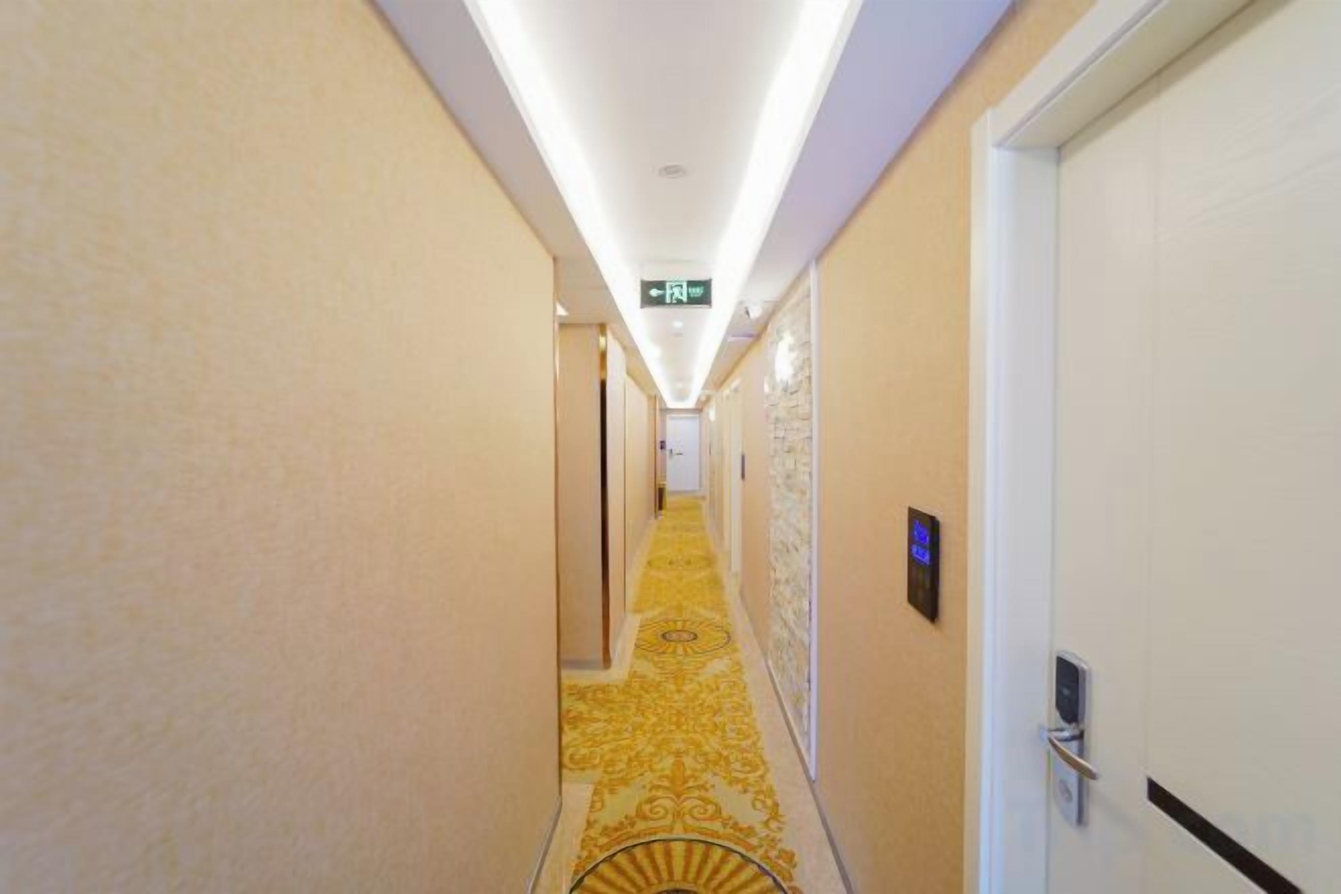 Un pasillo de hotel con alfombra estampada, una puerta con picaporte y un dispositivo fijado a la pared.