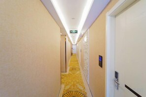A hotel hallway with a patterned carpet, a door with a handle, and a wall-mounted device. - Fuzhijia Business Hostel (Shanghai)
