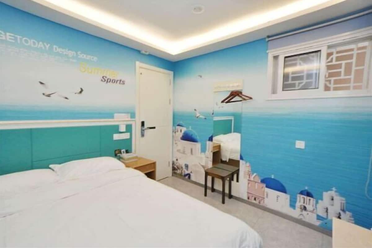 A bedroom with a bed, a nightstand, a wall-mounted TV, and a window with a view of the sea.