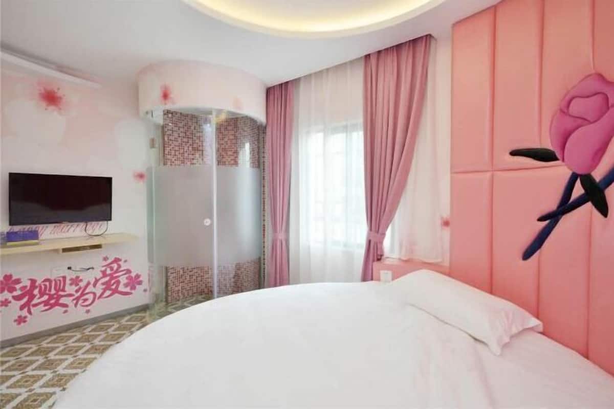 A bedroom with a bed, a TV, a pink wall with a rose decoration, and a sliding door.