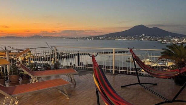 Un balcon avec un hamac, une table et une chaise, d’où l’on peut admirer un plan d’eau et une montagne lointaine.
