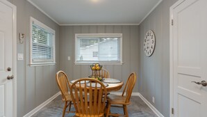 A dining area with a round table, four wooden chairs, a clock on the wall, and two windows with blinds. - Cozy & Tasteful 3Br Cottage Walkable to Downtown (Franklin)