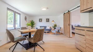 A modern kitchen with wooden cabinets, a dining table with chairs, and a sofa in the background.
