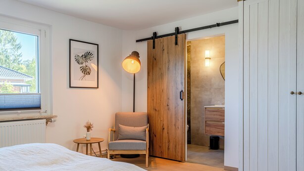 A bedroom with a bed, a chair, a wooden door, and a window.