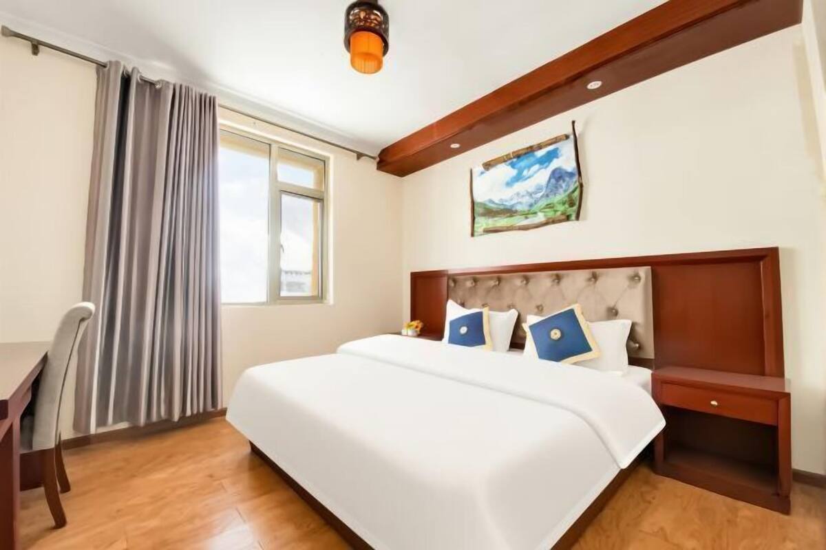 Une chambre d’hôtel avec un grand lit, un bureau, une chaise, une table de chevet et un tableau au mur.